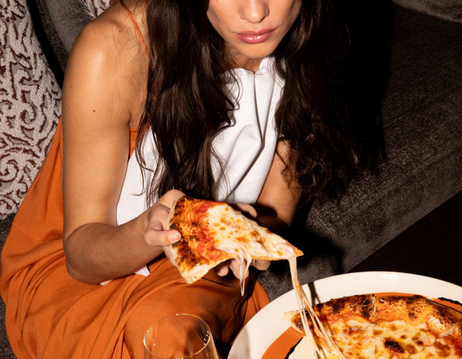Woman in an orange dress eating pizza.