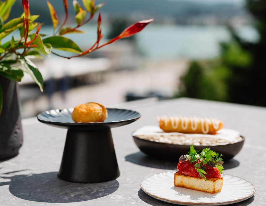 Pastries on marble plates on an outdoor table with water in the background