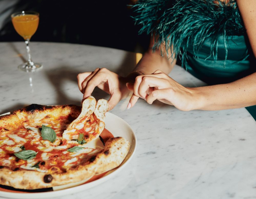 A woman in a green dress is enjoying a pizza on a marble plate