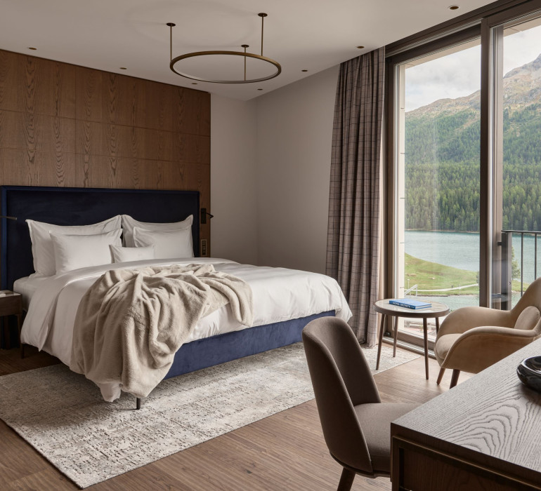 Cozy hotel room with a blue double bed and light bed sheets with a desk in front of it