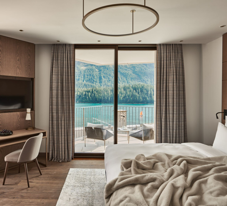 Light hotel room with a view at the lake in St. Moritz, a large double bed and a desk in the front