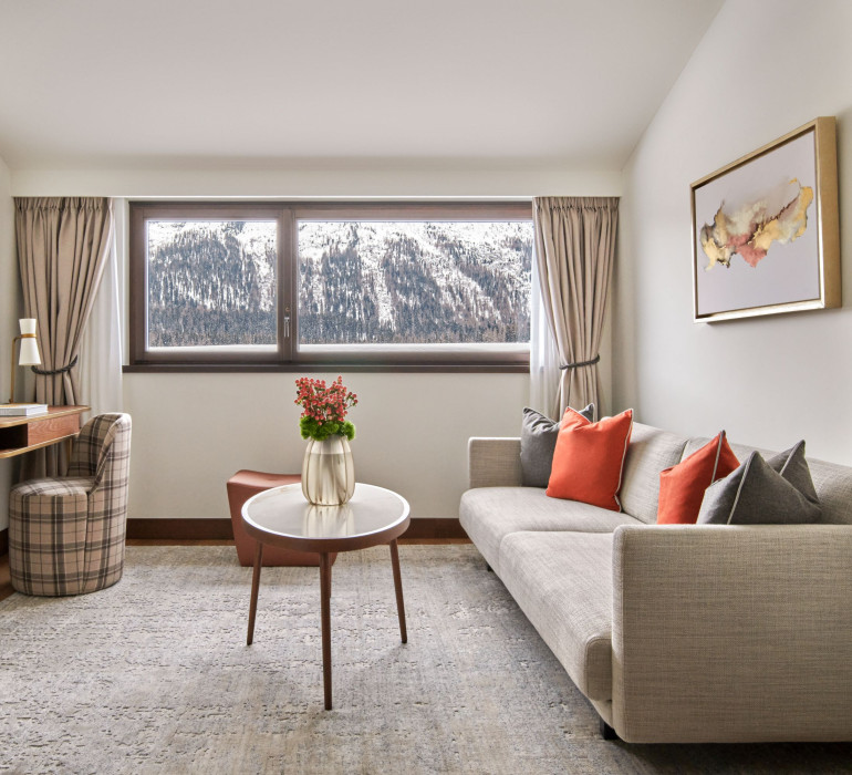 Grey carpet and a couch with a small round table infront of a window with a mountain view