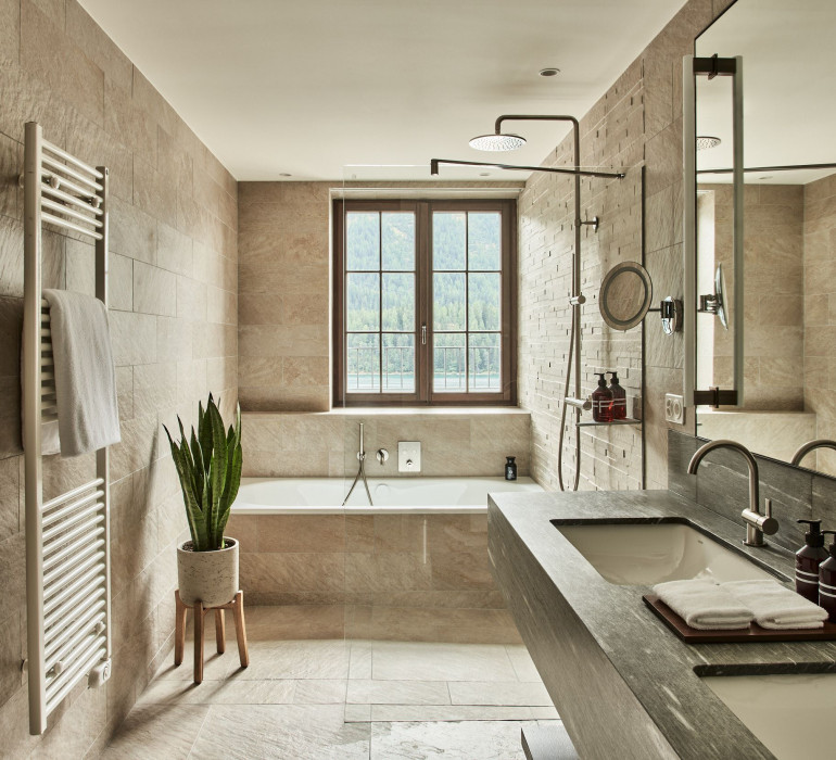 Large bathroom with stone tiles in neutral colors, a stone sink and a bath tub