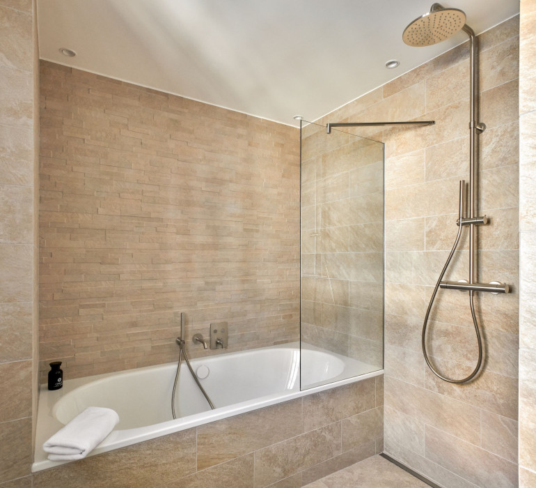 Large bath tub and a walk-in shower with nude tiles in a hotel bathroom