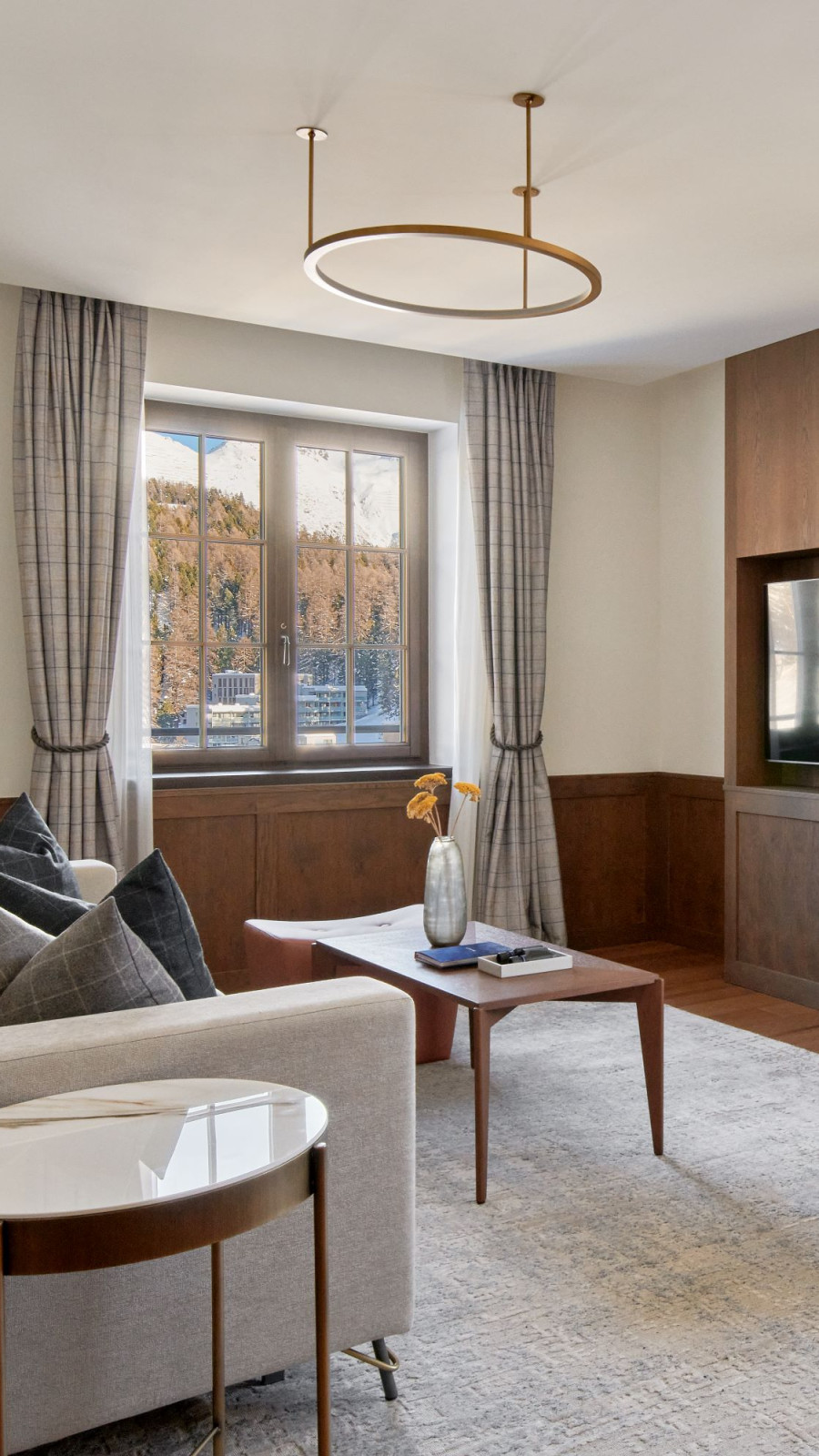 Grey couch and a wooden coffee table on a curtain next to a window with a mountain view