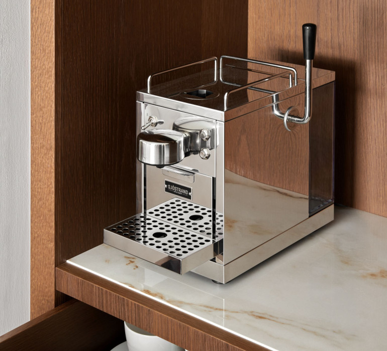 Small silver coffee machine on a marble plate in a brown cupboard