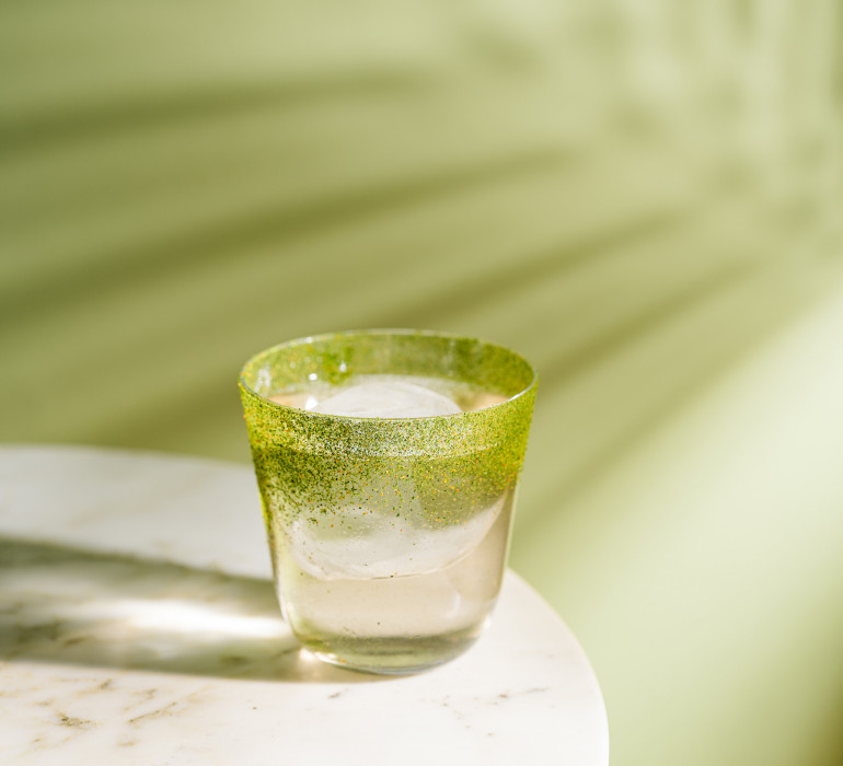 A glass of water placed on a marble plate in front of a green wall