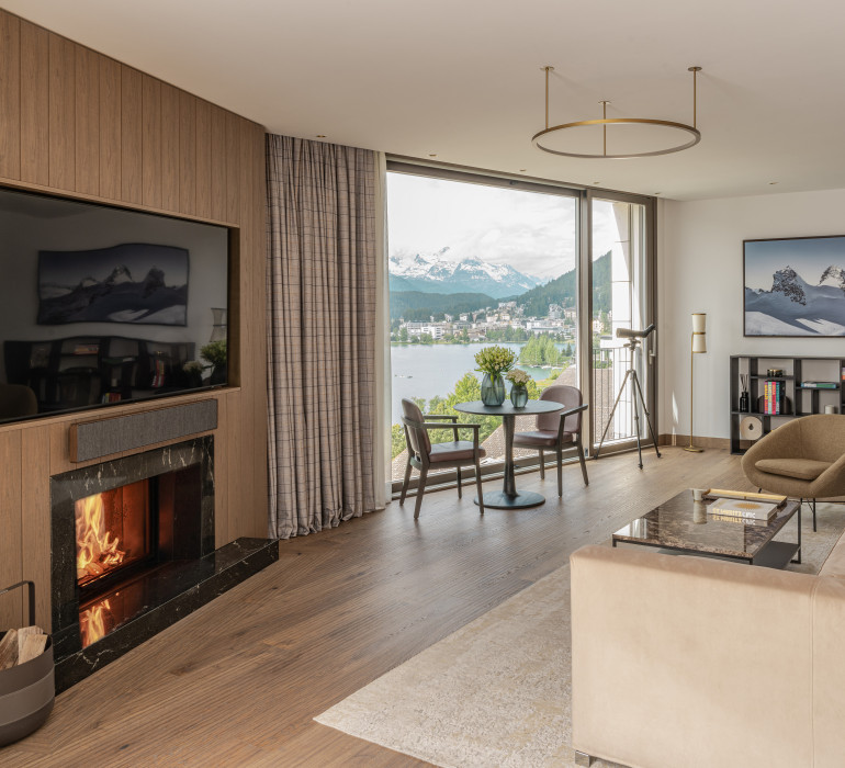 Großzügiger Wohnbereich im Penthouse mit Kaminfeuer, großem Fernseher und Tisch am Fenster mit Blick auf den See