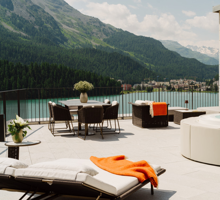 Großzügiger Wohnbereich im Penthouse mit Kaminfeuer, großem Fernseher und Tisch am Fenster mit Blick auf den See