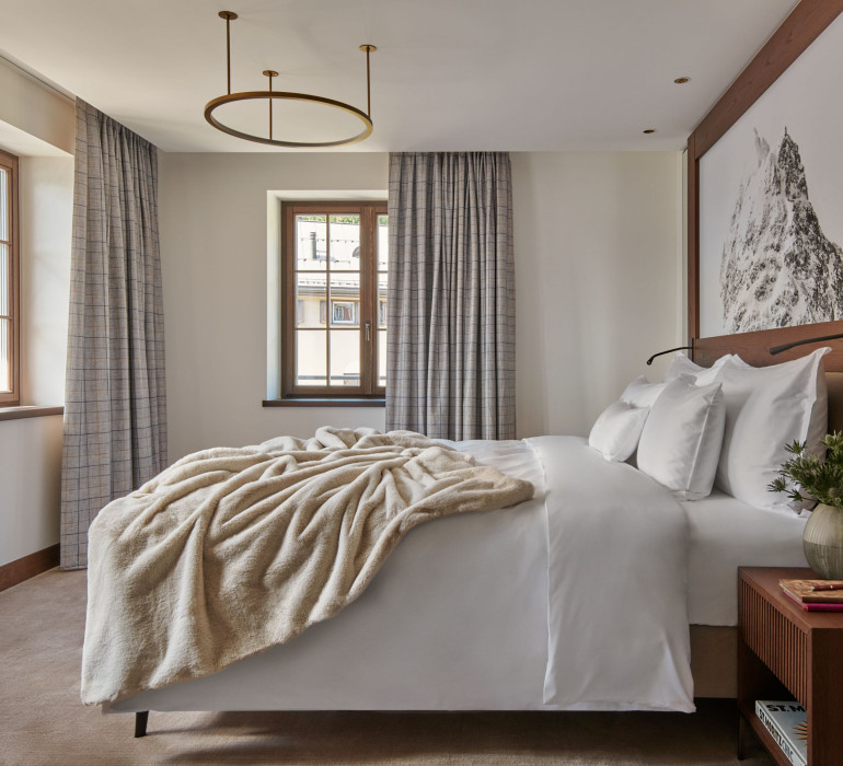 Elegant hotel room with a double bed, a fuzzy blanket and an alpine mountain painting above the head