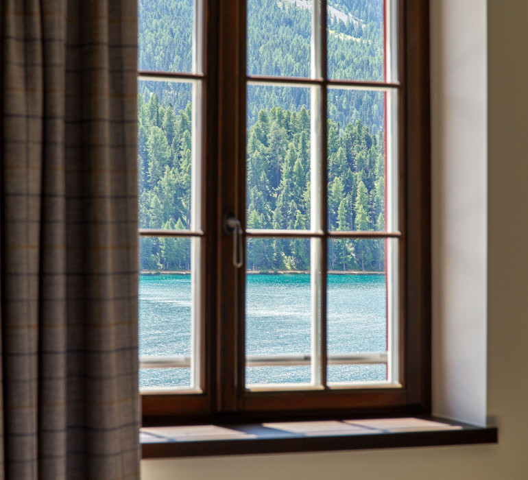 Details of a window with a grey curtain and a view at a sunny lake