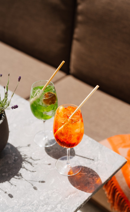 An Aperol Spritz and a green cocktail on a white table