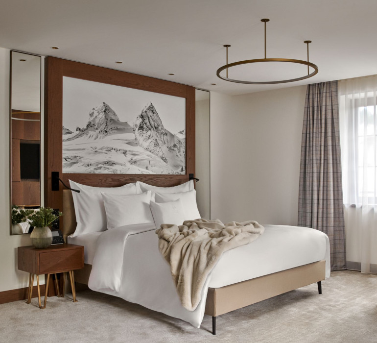 Hotel suite with a large double bed and a wooden wall with a mountain painting in the back