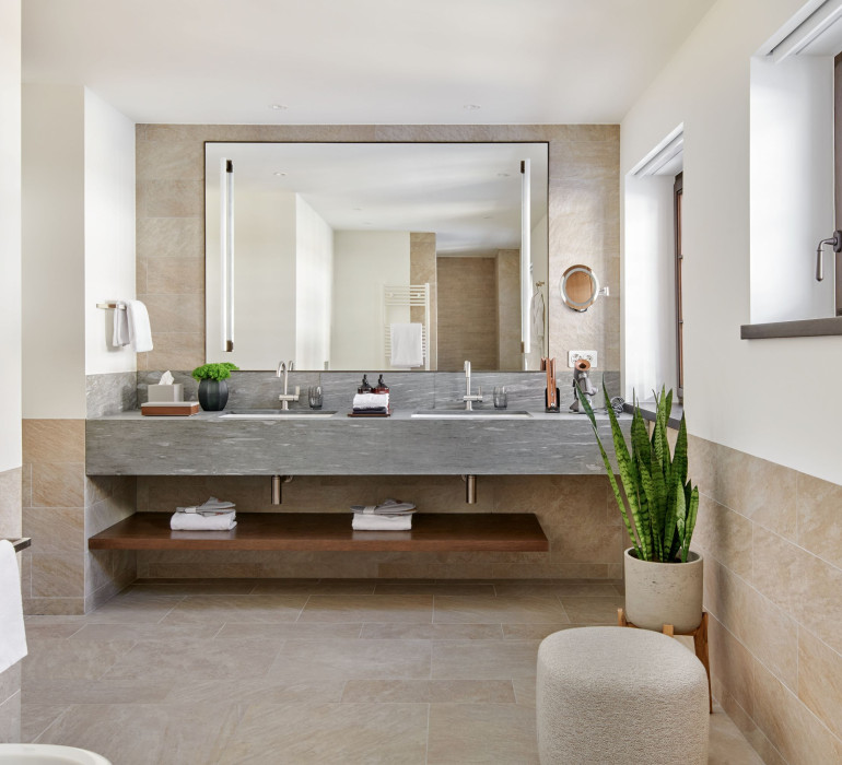 Modern bathroom with a large mirror, two sinks with grey stone and some plants