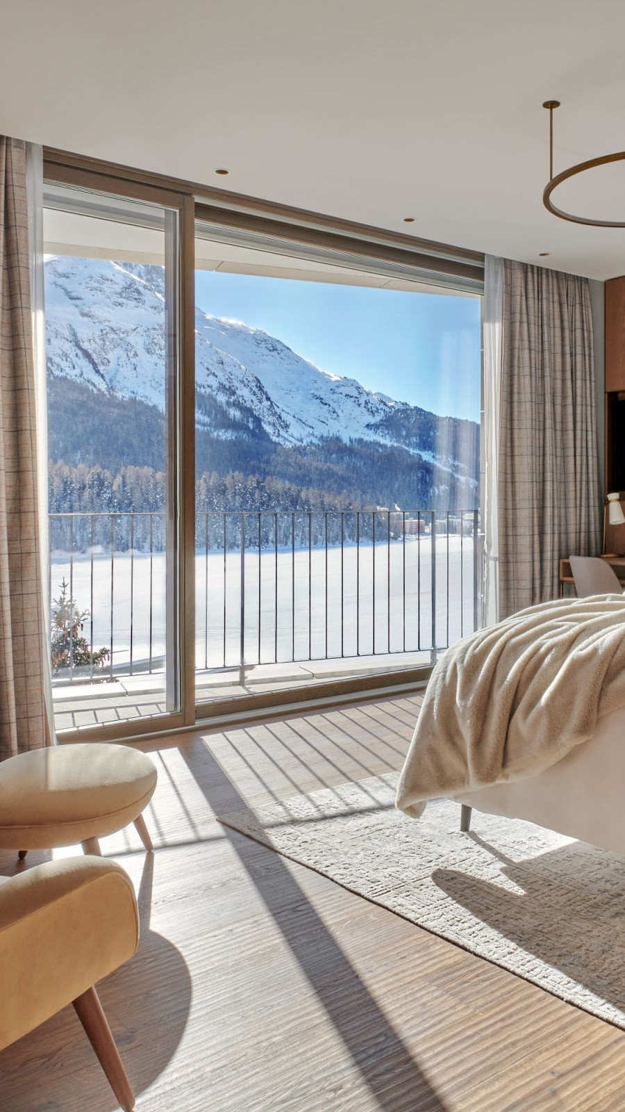 Panoramic suite in St. Moritz with a view at the mountains, a cozy double bed and two arm chairs infront of the window