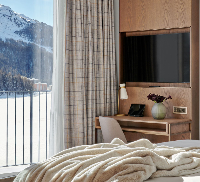 Fluffy blanket on a hotel bed and a small desk next to the window with a mountain view