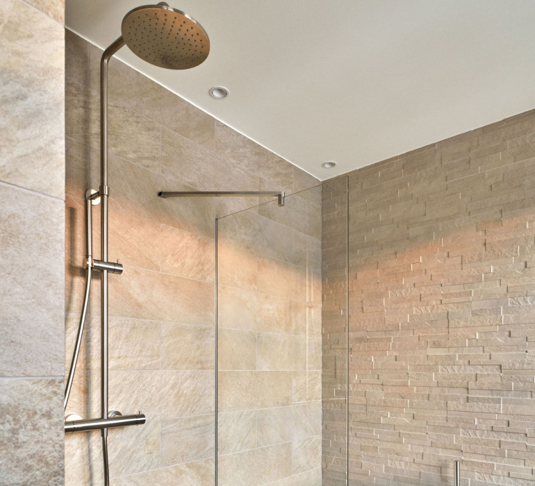 Bright walk-in shower with beige tiles and a glass wall on the side