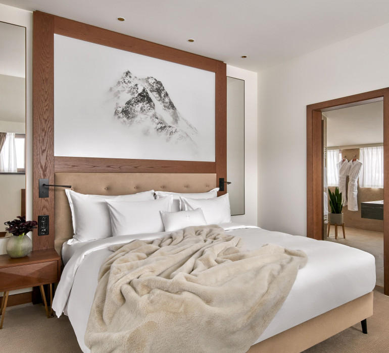 Elegant hotel room with a double bed, a fuzzy blanket and an alpine mountain painting above the head