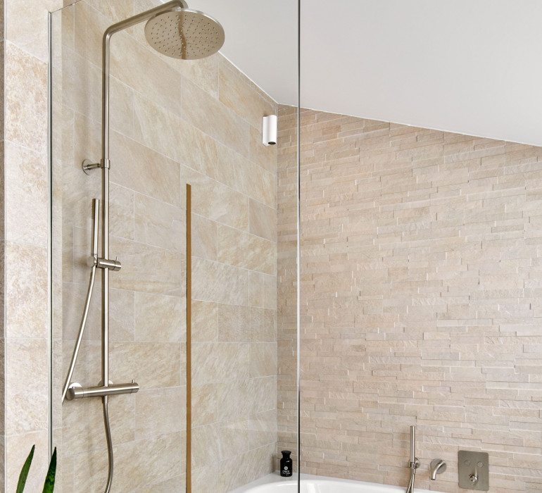 Details of a shower with a glass door and a bath tub on the side