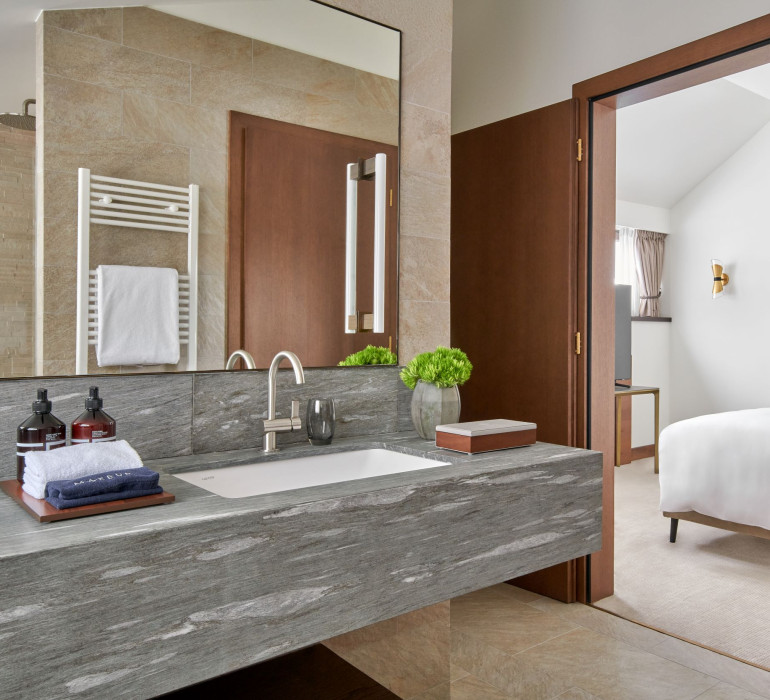 Open bathroom of a hotel suite with stone sinks, lotions and small towels