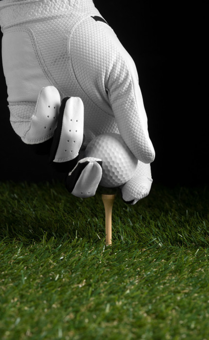 A hand in a glove is placing a golf ball at the form